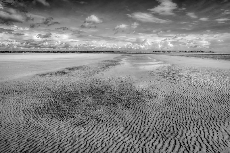 Black and white ripples in wet sand beneath a dramatic coastal sky.