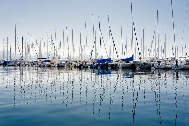 Sailboat masts and their reflections in still blue water.